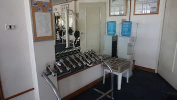 A room with a weight bench, a mirror, a water dispenser, and a door with a bulletin board.