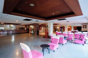 Un vestíbulo amplio con una mesa de recepción, una estatua y sillones rosados dispuestos para sentarse.