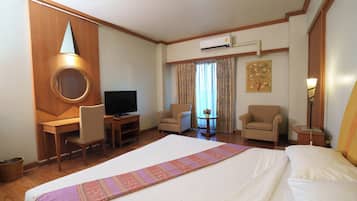 A hotel room with a large bed, a desk with a television, two armchairs, and a small table with a vase.