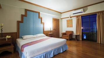 Quarto de hotel com cama, cadeira, escrivaninha, ar condicionado e vista da cidade à noite.
