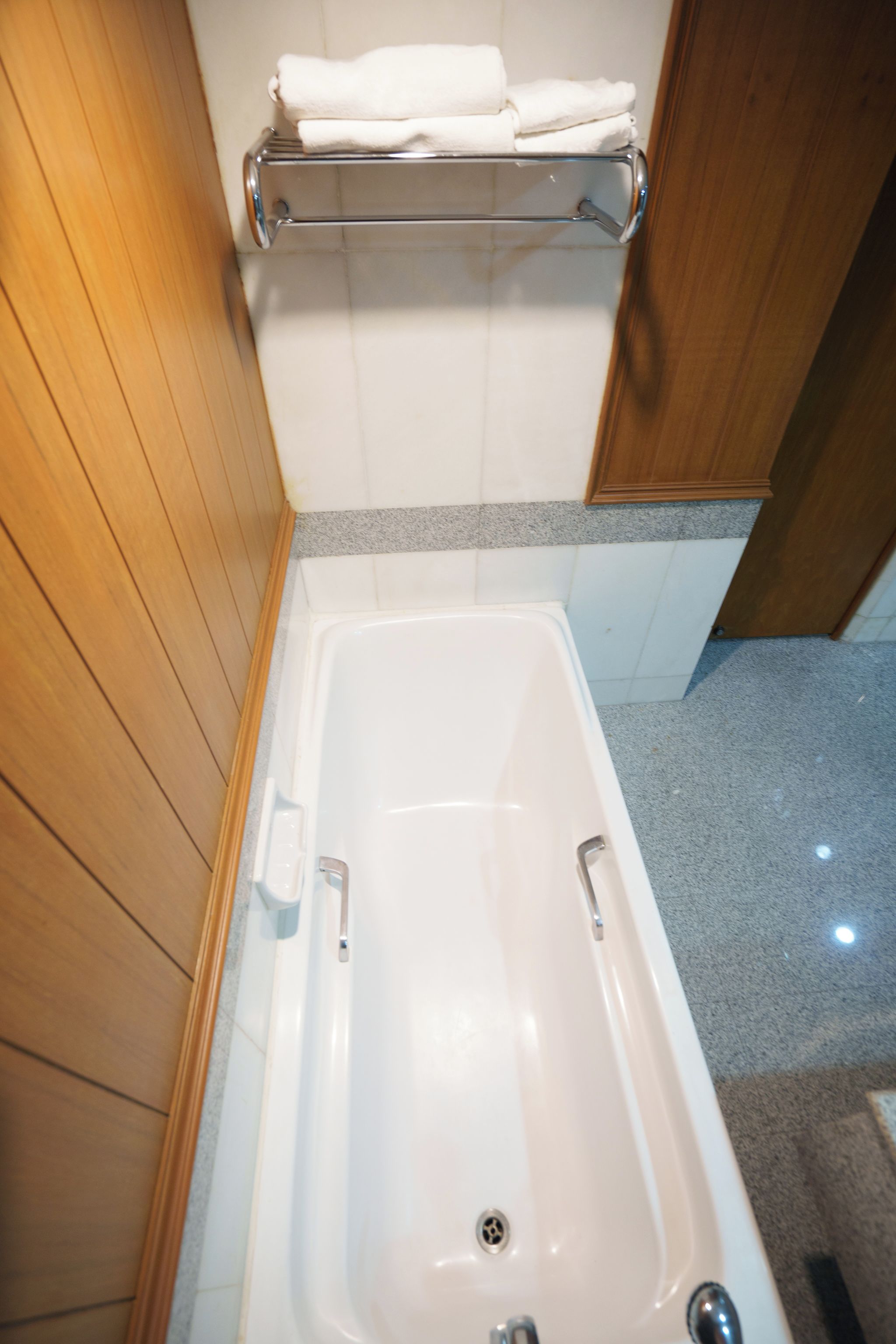 Un baño con una bañera blanca, un perchero con toallas dobladas y paneles de madera en las paredes.