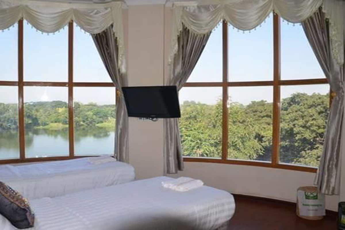 A bedroom with two beds, a TV mounted on the wall, and large windows offering a view of a lake and forest.