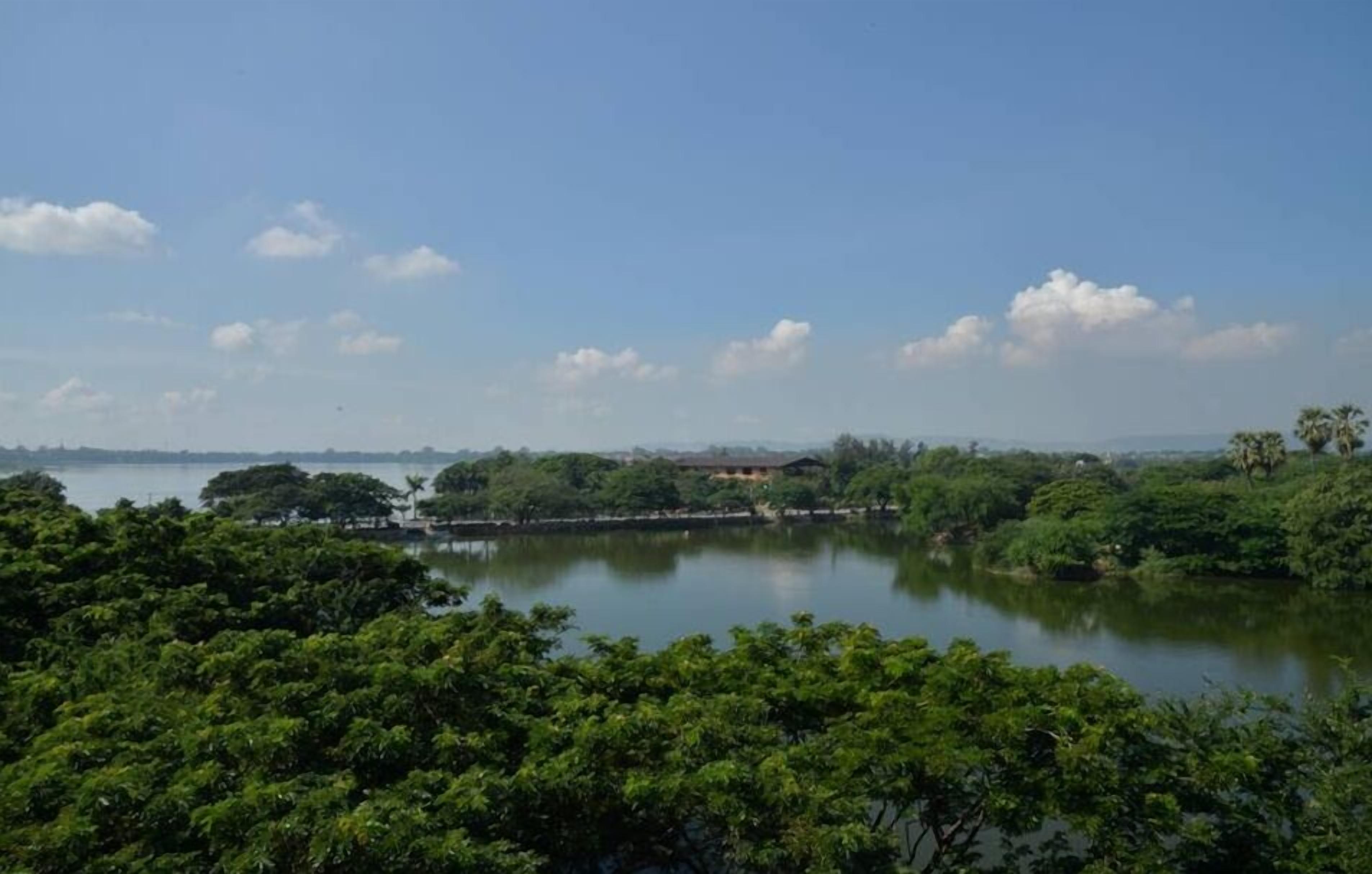 A lake surrounded by dense greenery and a clear sky.