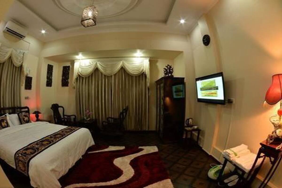 A hotel room with a bed, a desk, a chair, a TV, and a red lamp.