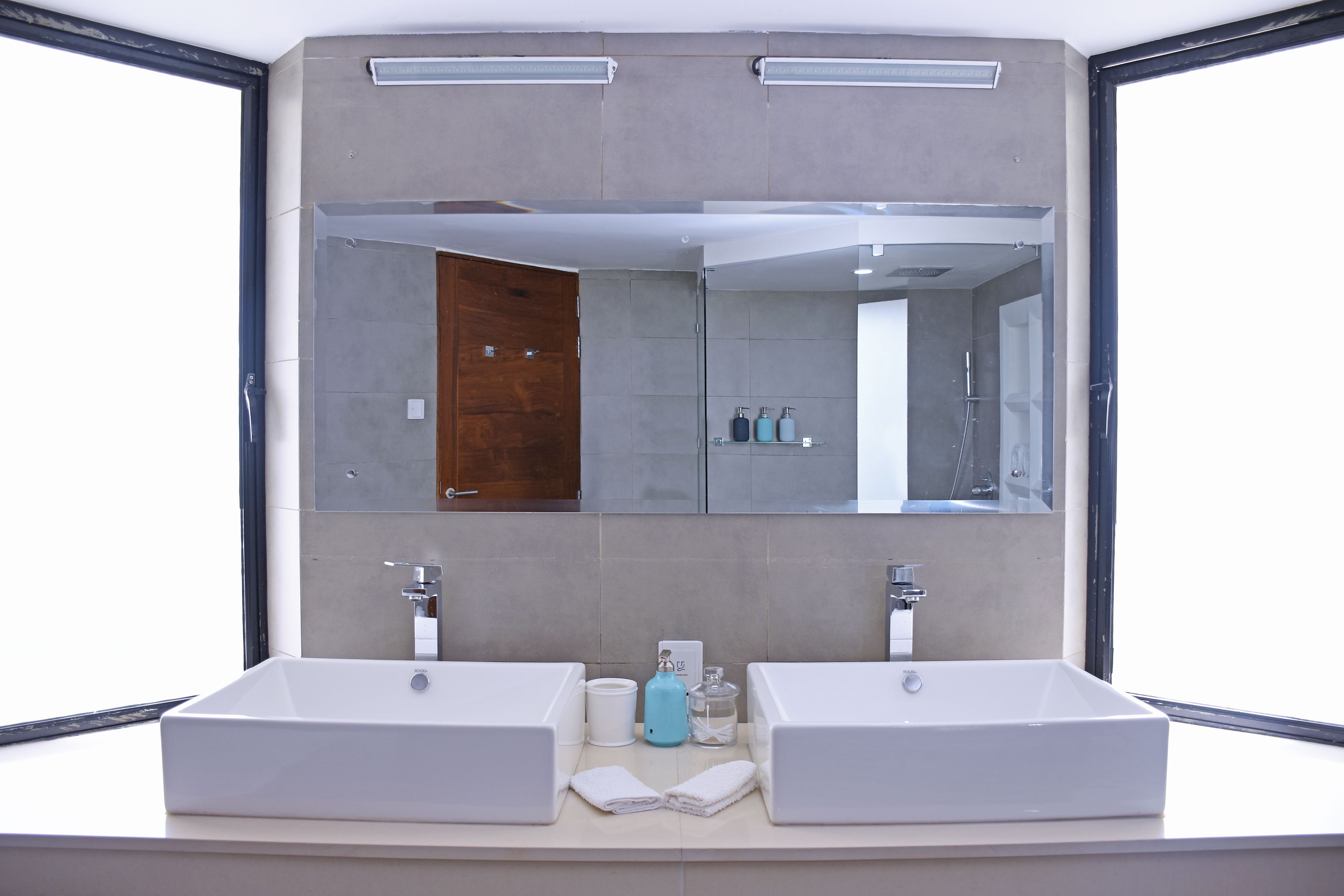 A modern bathroom with two sinks, a large mirror, and a shower visible in the reflection.