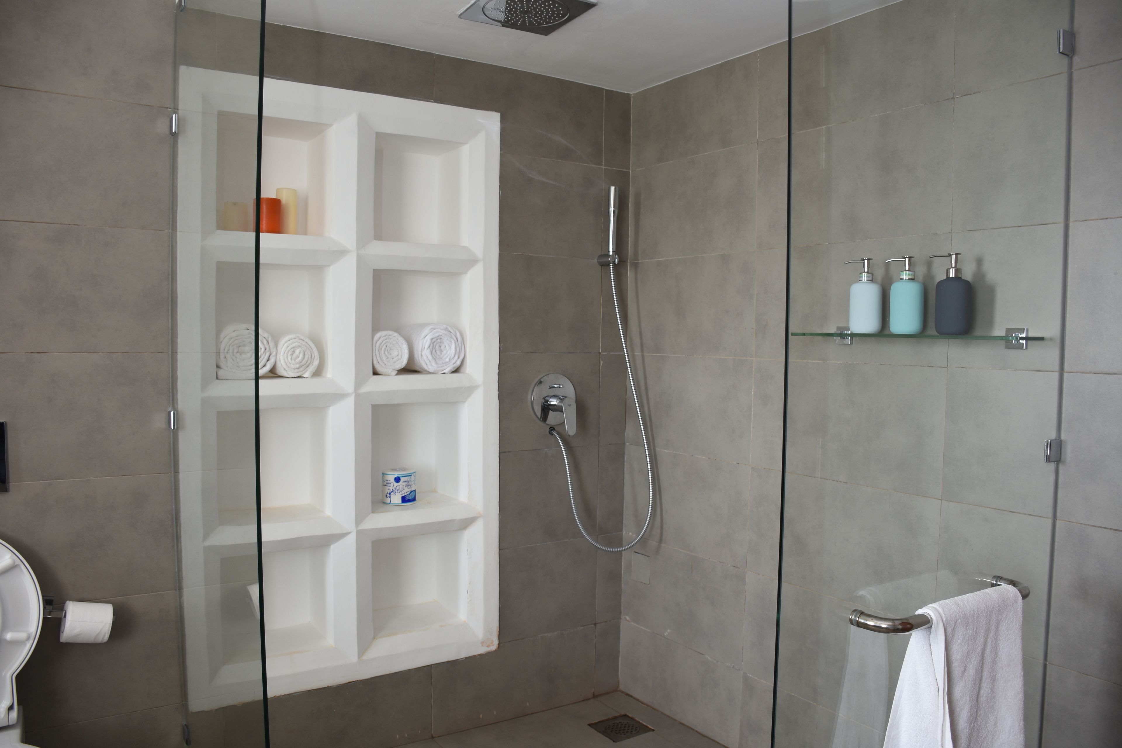 A modern bathroom with a glass-enclosed shower, a white vanity with shelves, and a glass shelf with toiletries.
