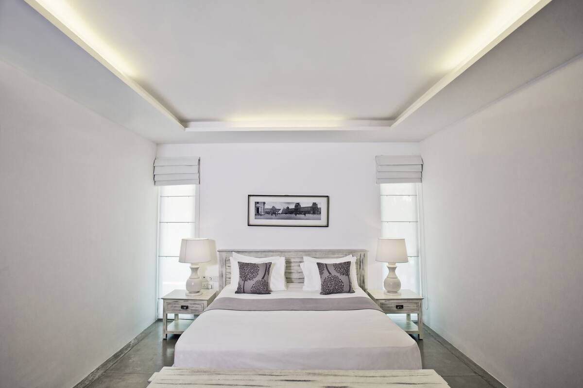 Une chambre à coucher moderne avec un grand lit, des lampes de chevet, un tableau encadré au mur et un luminaire au plafond.