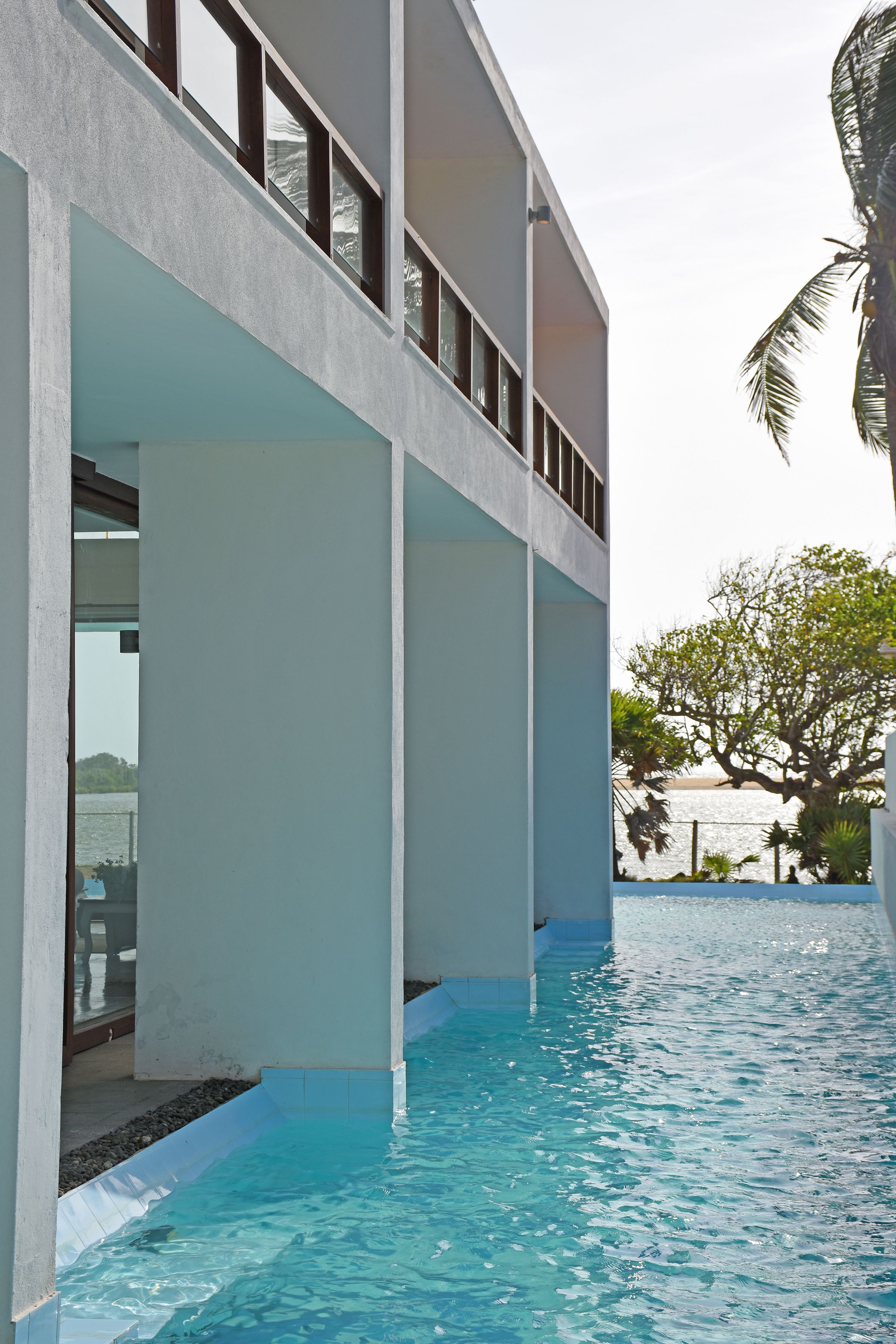 A modern building with a pool, large windows, and a view of the water.