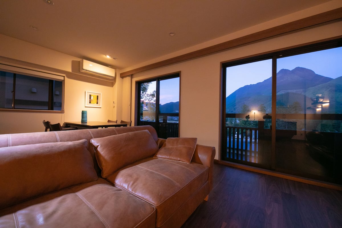 Ein modernes Wohnzimmer mit einer Ledersofa, einem Esstisch und Bergblick durch große Fenster.