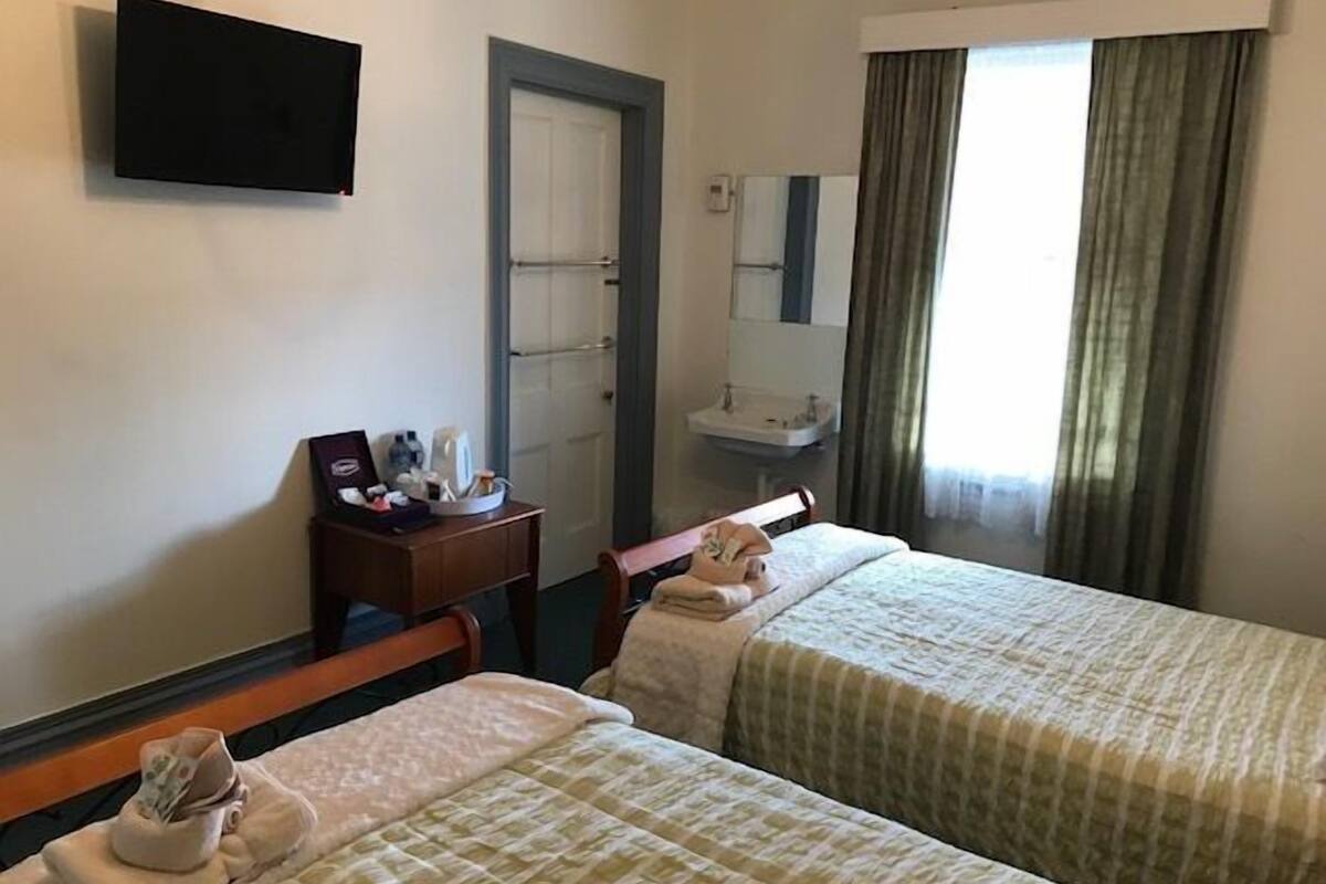 Hotellihuone, jossa on kaksi sänkyä, työpöytä, jossa on hygieniatarvikkeita, peili ja ikkuna, jossa on verhot.