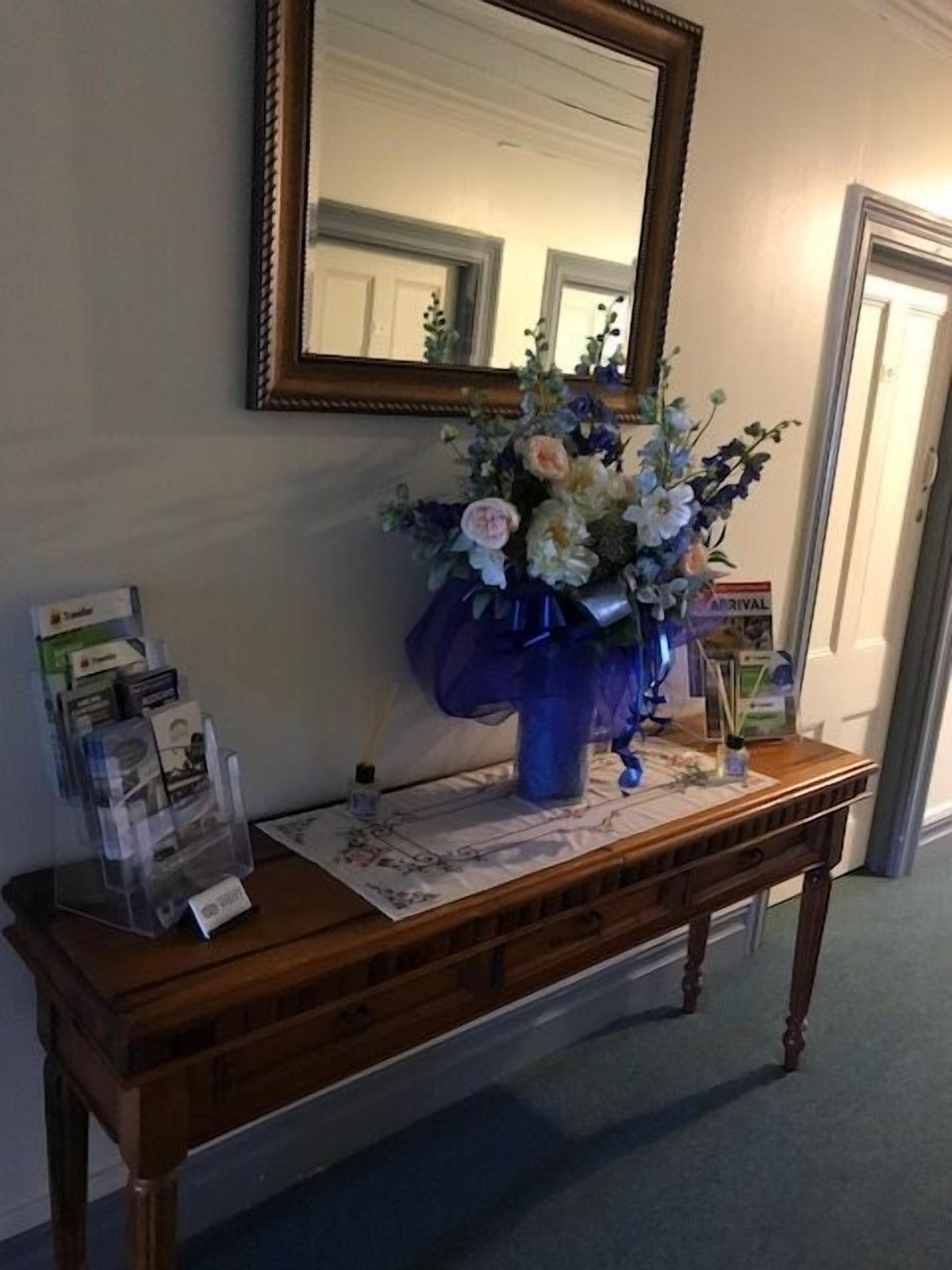 A wooden console table with a vase of flowers, a magazine rack, and a framed mirror on the wall.