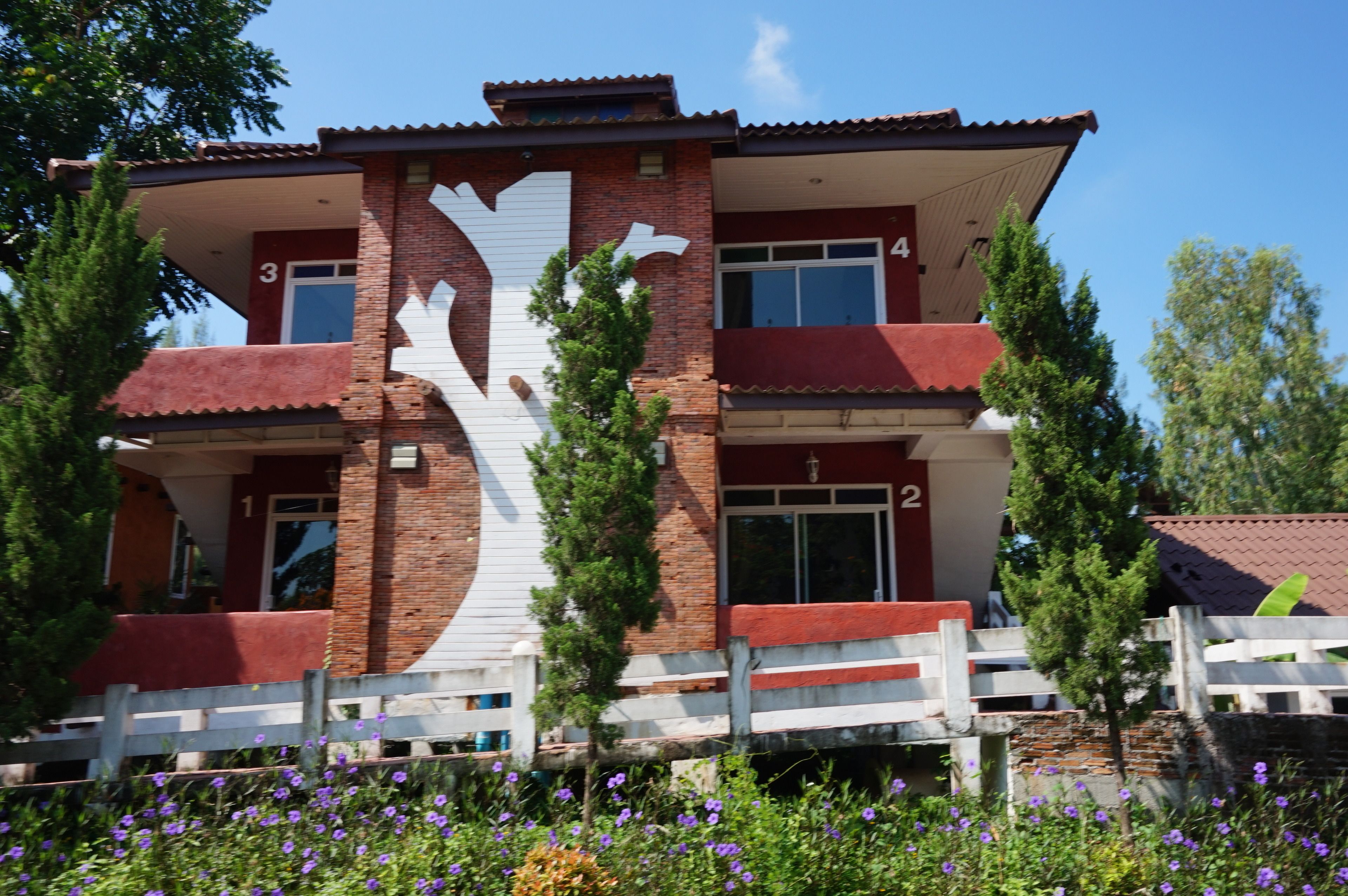 A two-story building with a distinctive white tree-like design on the facade, numbered rooms, and a white fence in front.
