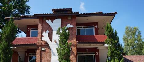 A two-story building with a distinctive white tree-like design on the facade, numbered rooms, and a white fence in front.