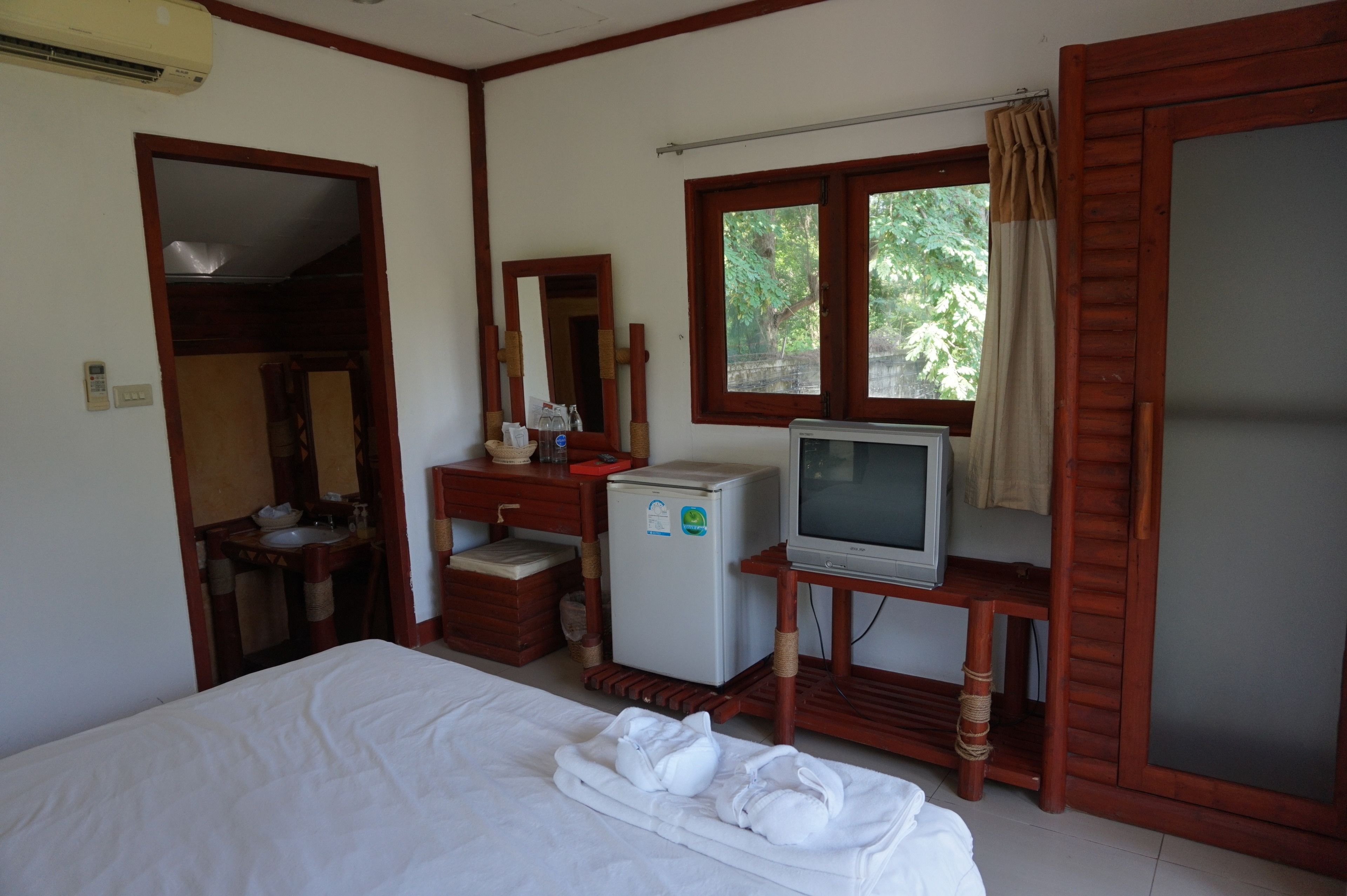 A hotel room with a bed, a television, a small refrigerator, a mirror, and a window with curtains.
