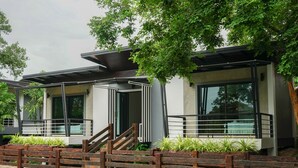 Een modern gebouw met grote ramen, een houten brug en groen.