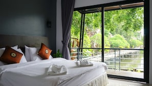 Hotelkamer met een groot bed, wit beddengoed en uitzicht op een tuin en een waterpartij door een groot raam.