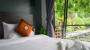 Een hotelkamer met een bed, uitzicht op groen en een balkonhek.