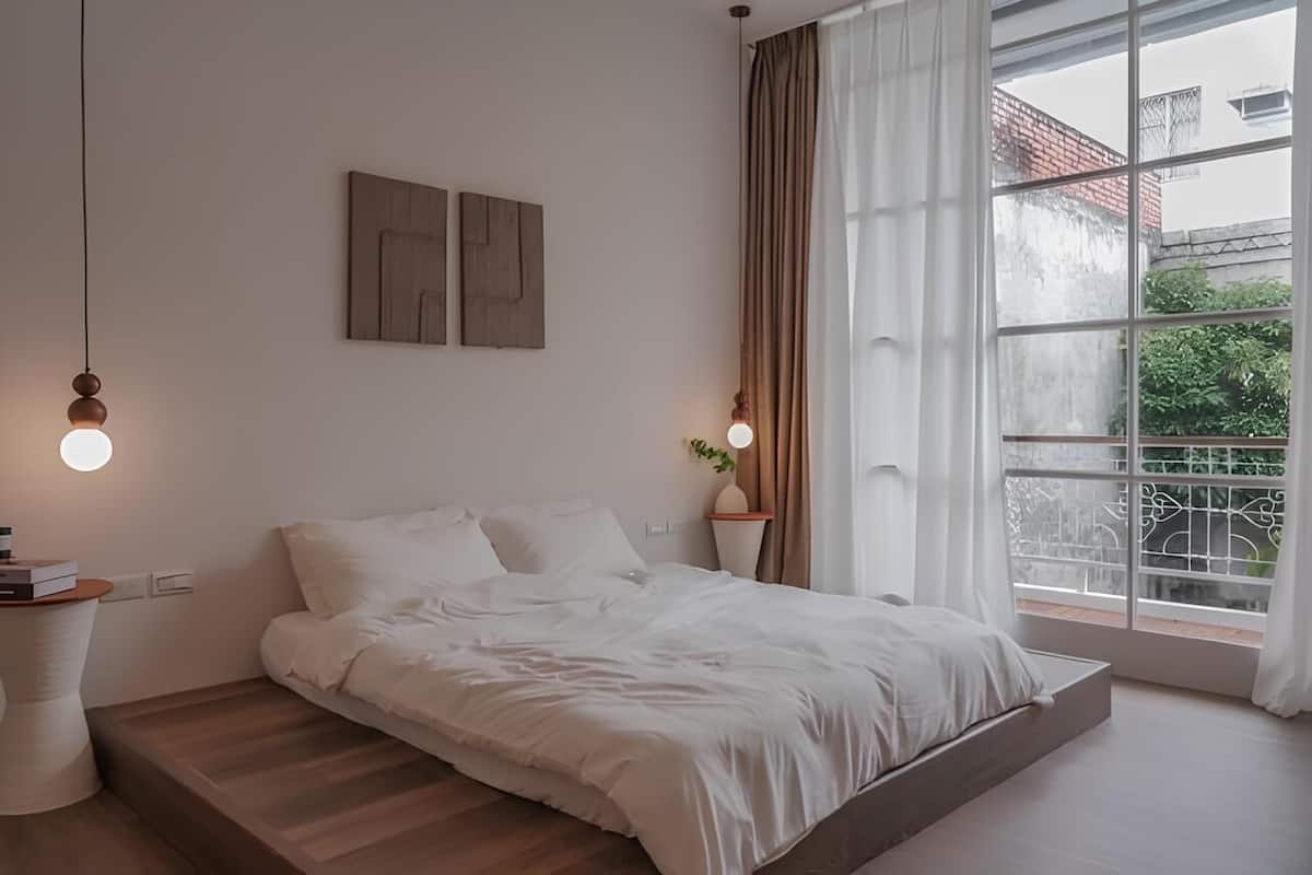 Un dormitorio con cama, mesitas de noche, ventana con cortinas y vistas al exterior.