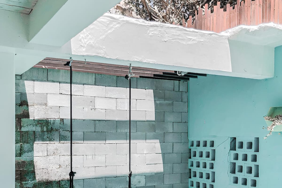 Una piscina con piso de baldosas y escalones para entrar. Hay postes metálicos en la piscina, y una pared de ladrillo con una sección de baldosas blancas.
