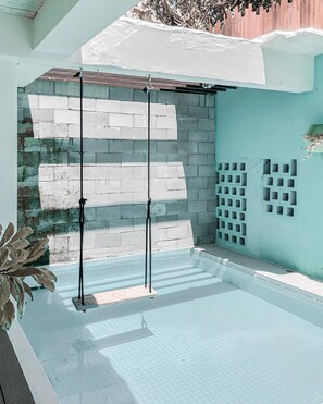 Une piscine dont le fond est carrelé et qui est accessible par des marches. On y trouve des poteaux métalliques, ainsi qu’un mur en briques avec une partie recouverte de carreaux blancs.