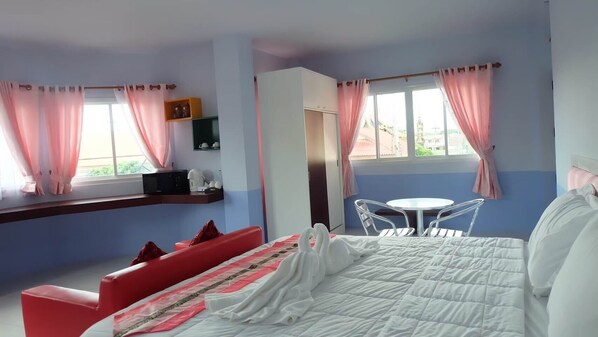 A bedroom with a bed, a red sofa, a small table, and a window with curtains.