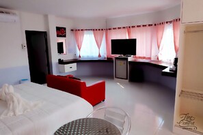 A hotel room with a bed, a red sofa, a small table, a TV, and a desk with a computer.