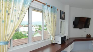 Een kamer met een groot raam, een wandtelevisie, een magnetron op het aanrecht en uitzicht op de stad.