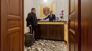 A reception area with a wooden reception desk, a coat check, and a patterned floor. - Vinohradský dům (Prague)