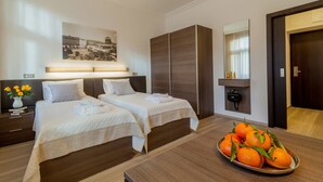 A hotel room with two beds, a large wardrobe, a bedside table with a vase of flowers, and a tray of oranges. - Vinohradský dům (Prague)