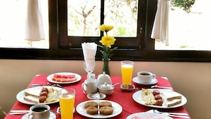 A breakfast table with plates of food, a vase with yellow flowers, and a window view. - Morning Glory Inn (Kalaw)