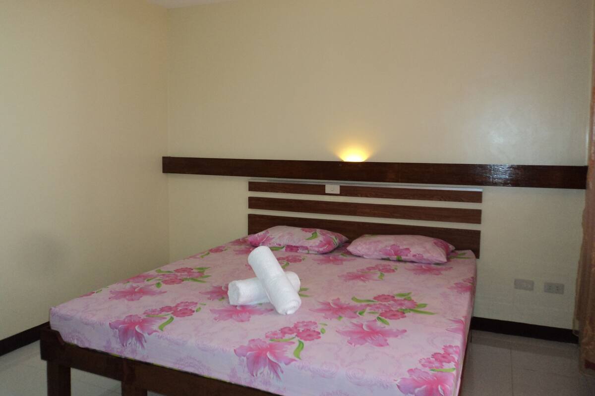 A single bed with a floral bedspread, wooden headboard, and two pillows.