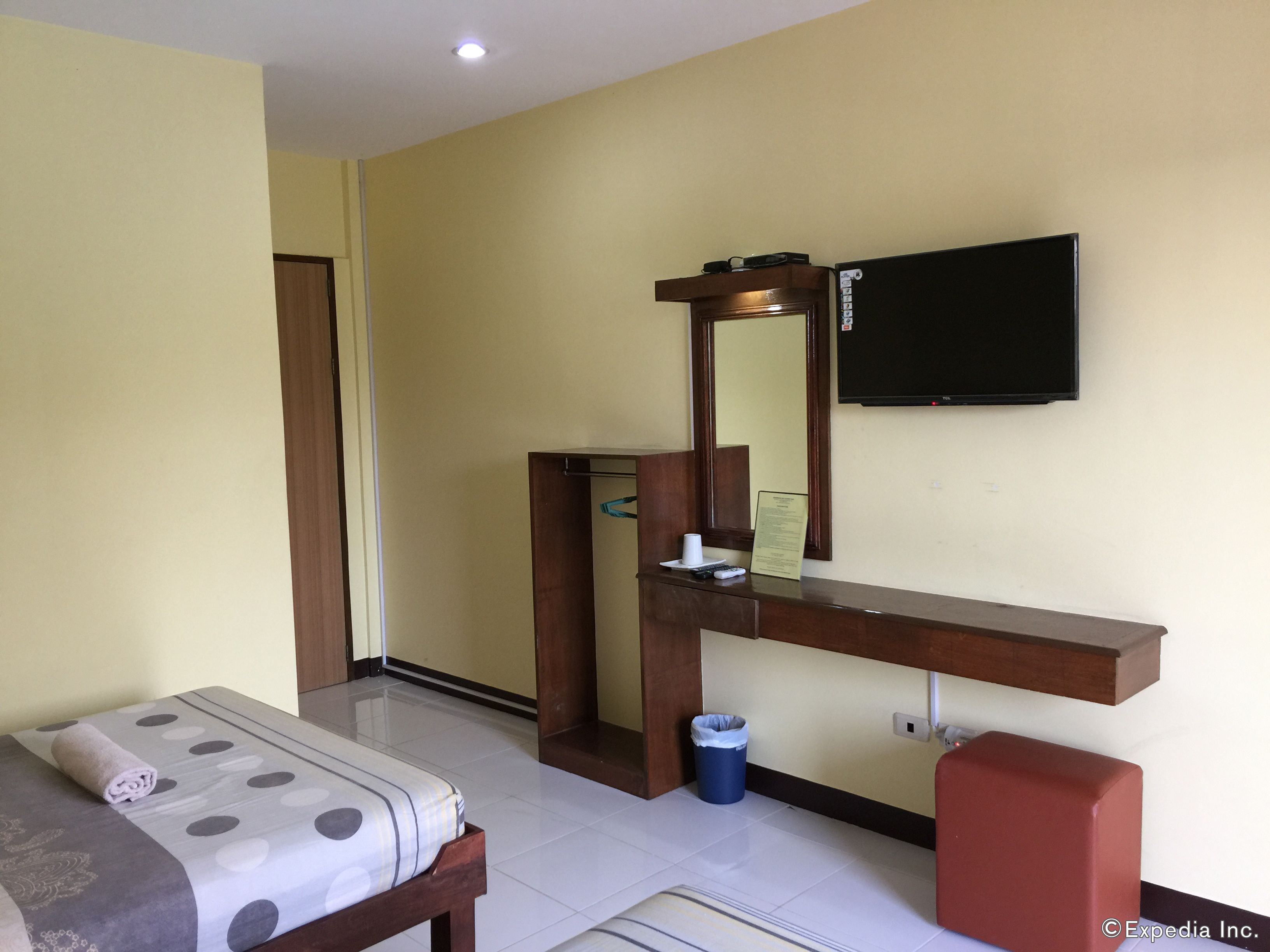 A hotel room with a bed, a desk with a mirror, a television, and a trash bin.