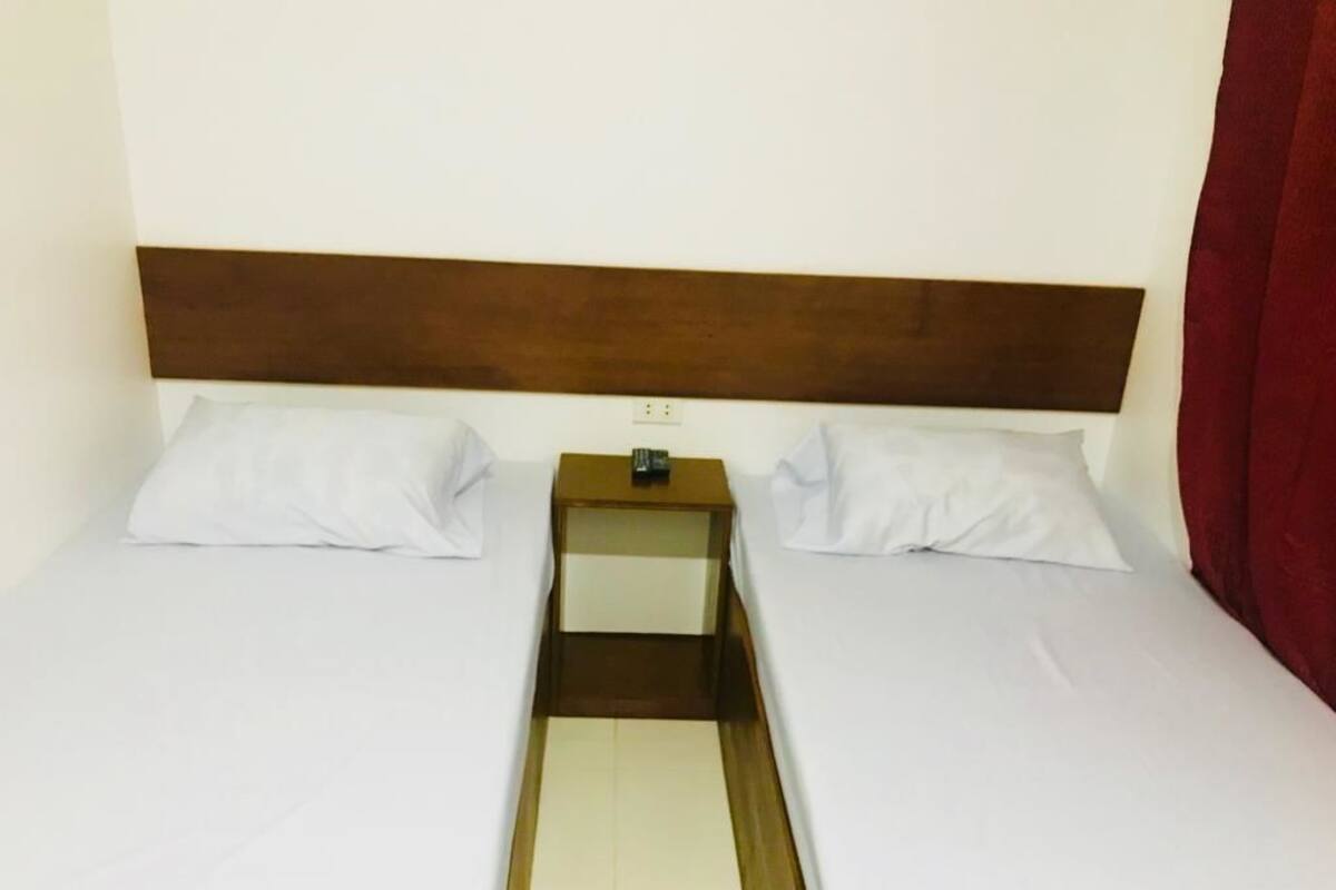 A twin room with two single beds, a wooden headboard, a small bedside table, and a red curtain.