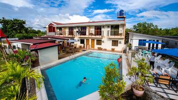 A hotel with a swimming pool, outdoor seating, and a two-story building with balconies.