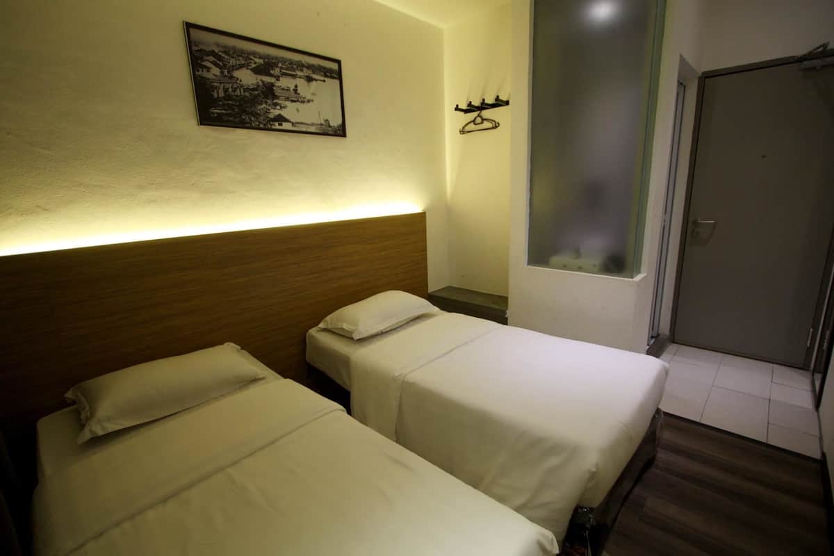 A hotel room with two single beds, a wooden headboard, a framed picture on the wall, and a door with a frosted glass window.