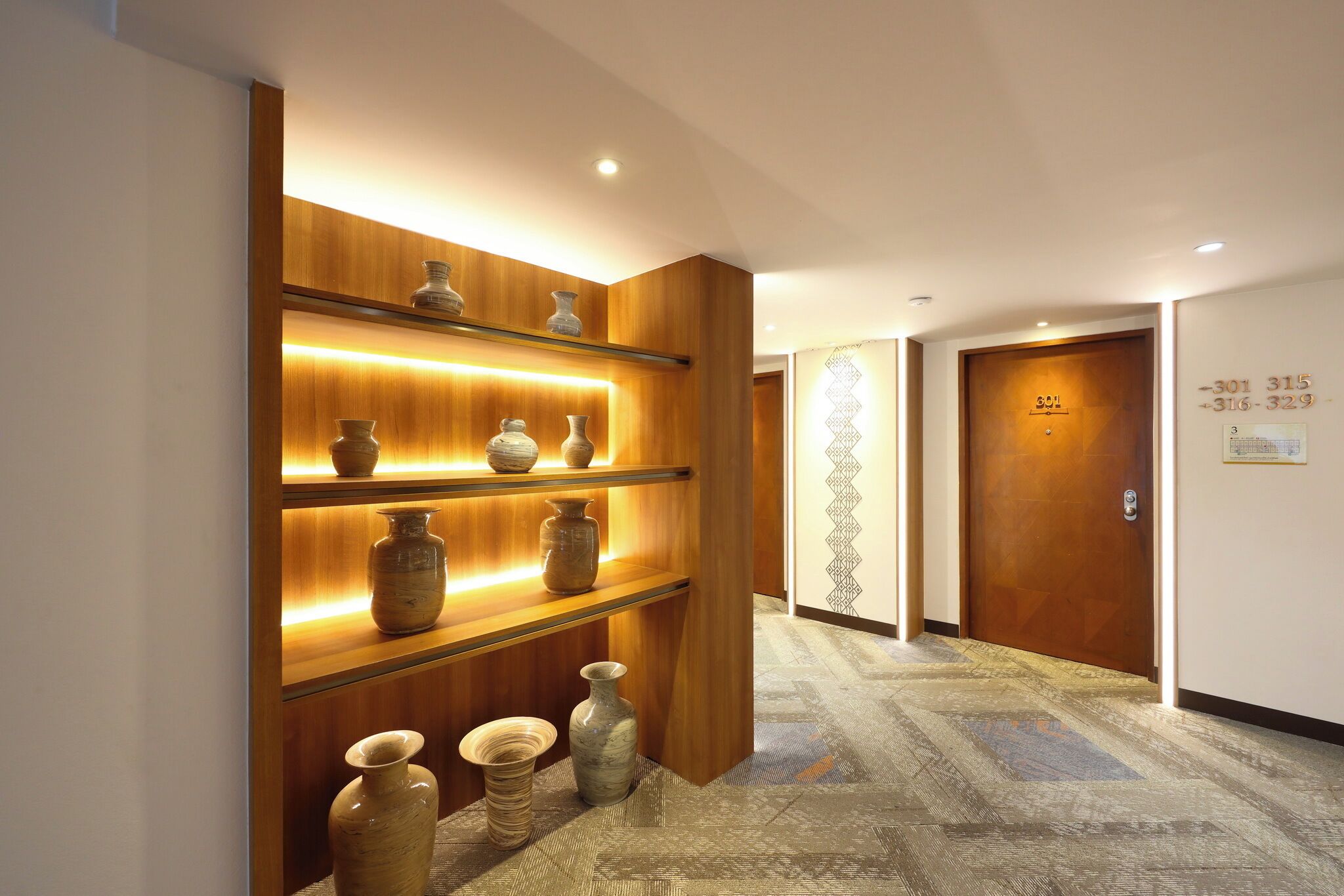 A hallway with wooden shelves displaying vases, a patterned carpet, and a door with contact numbers.
