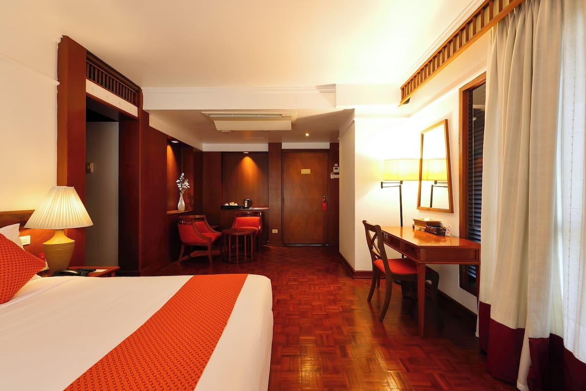 Une chambre d’hôtel avec un lit, un bureau, une chaise, une petite table et une lampe.