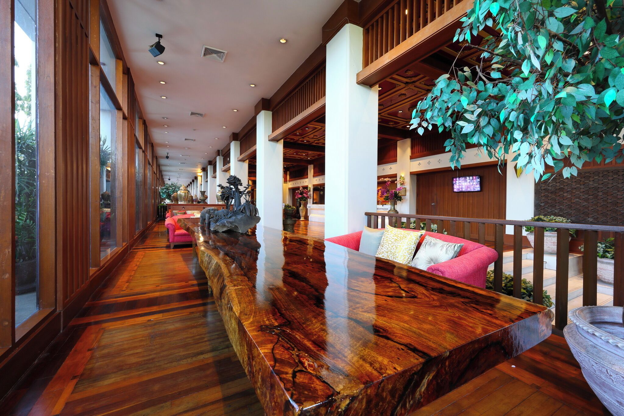 A spacious lobby with a long wooden reception desk, large windows, and a hanging plant.
