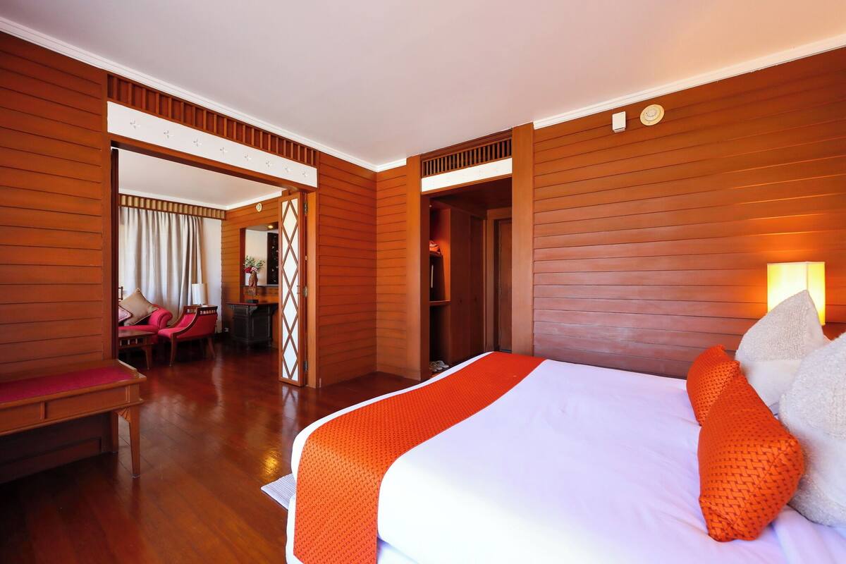Une chambre d’hôtel avec un grand lit, des murs en bois, un coin salon avec des fauteuils et un miroir.