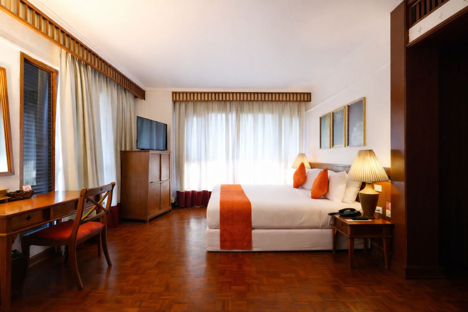 A hotel room with a bed, a desk, a chair, a television, and a lamp.