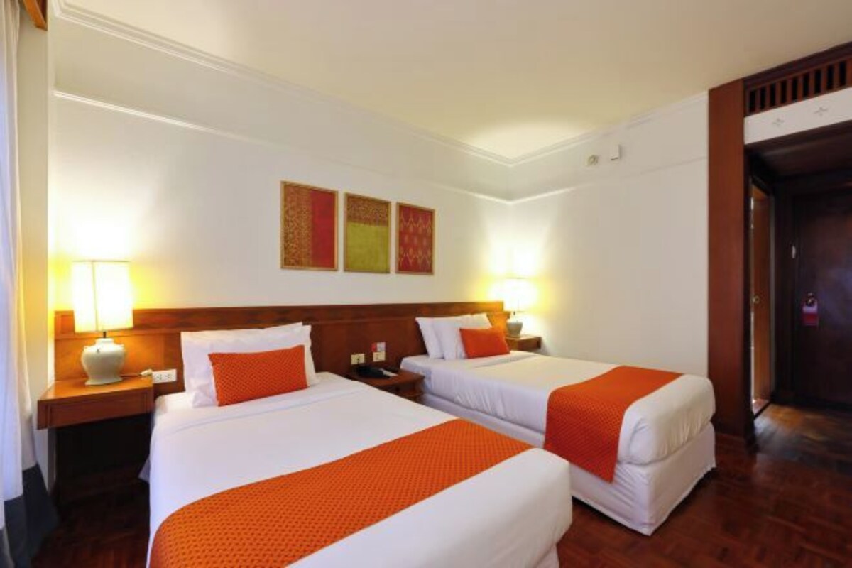 A hotel room with two beds, each with a white and orange bedspread, a wooden headboard, and a nightstand with a lamp.