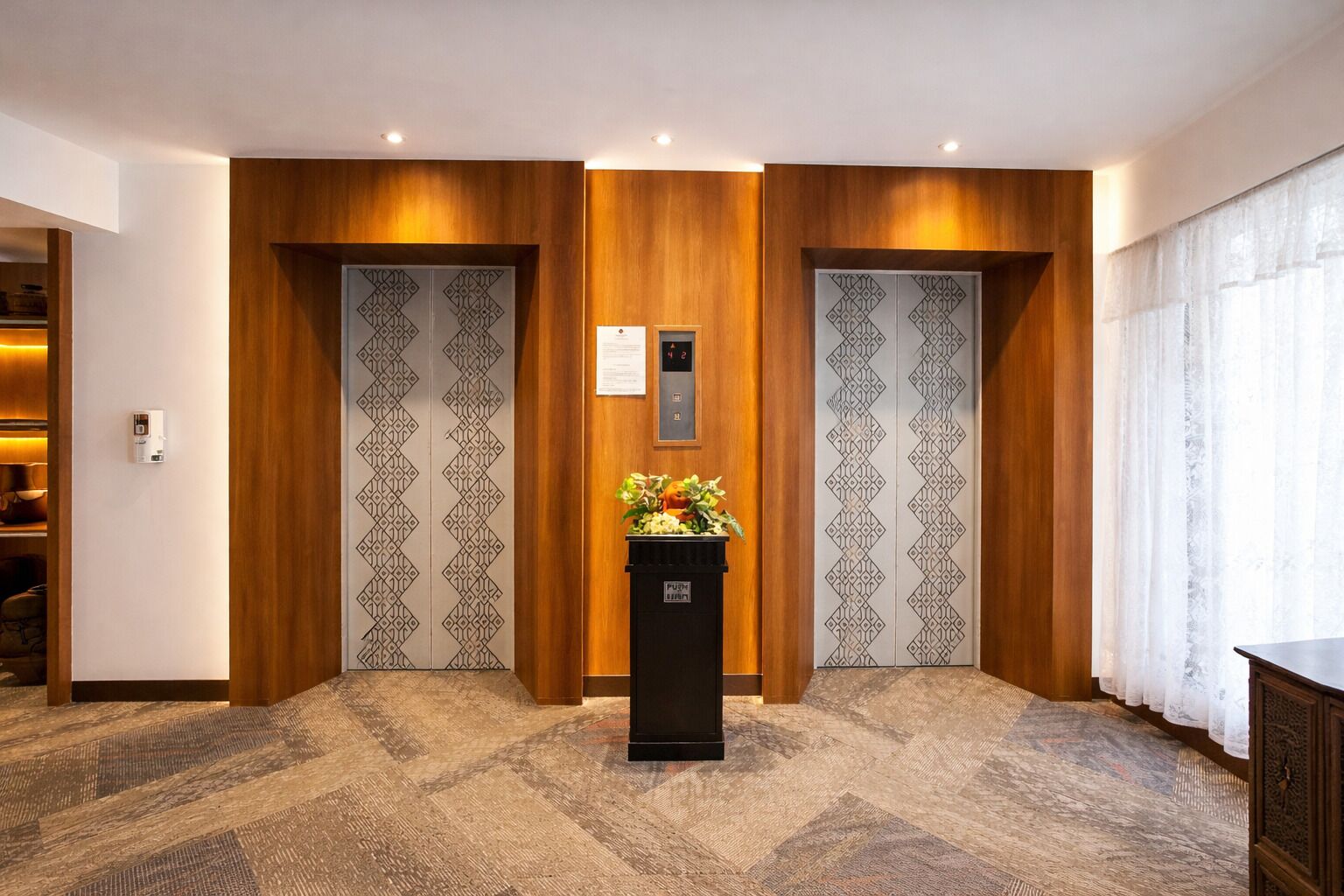 Un vestíbulo de hotel con dos ascensores, un mostrador de recepción y una alfombra estampada.