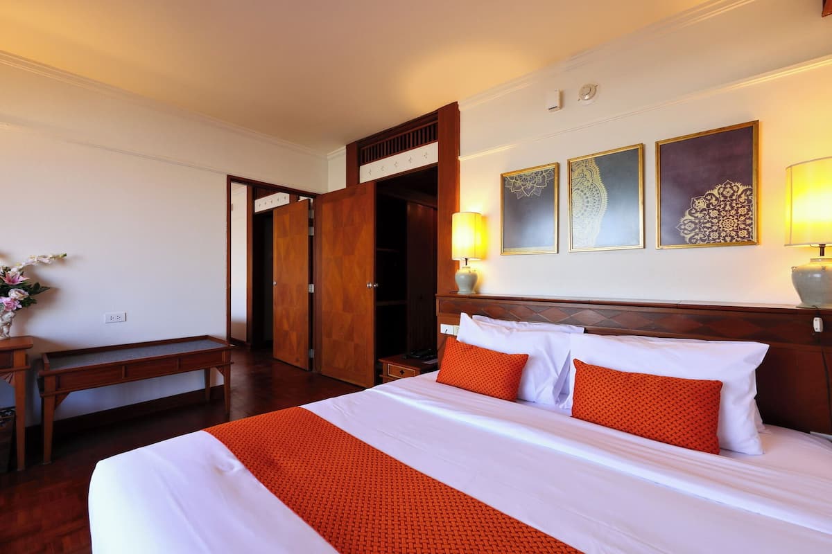 Une chambre d’hôtel comprenant un lit, des lampes de chevet, un bureau en bois, un banc et une armoire.