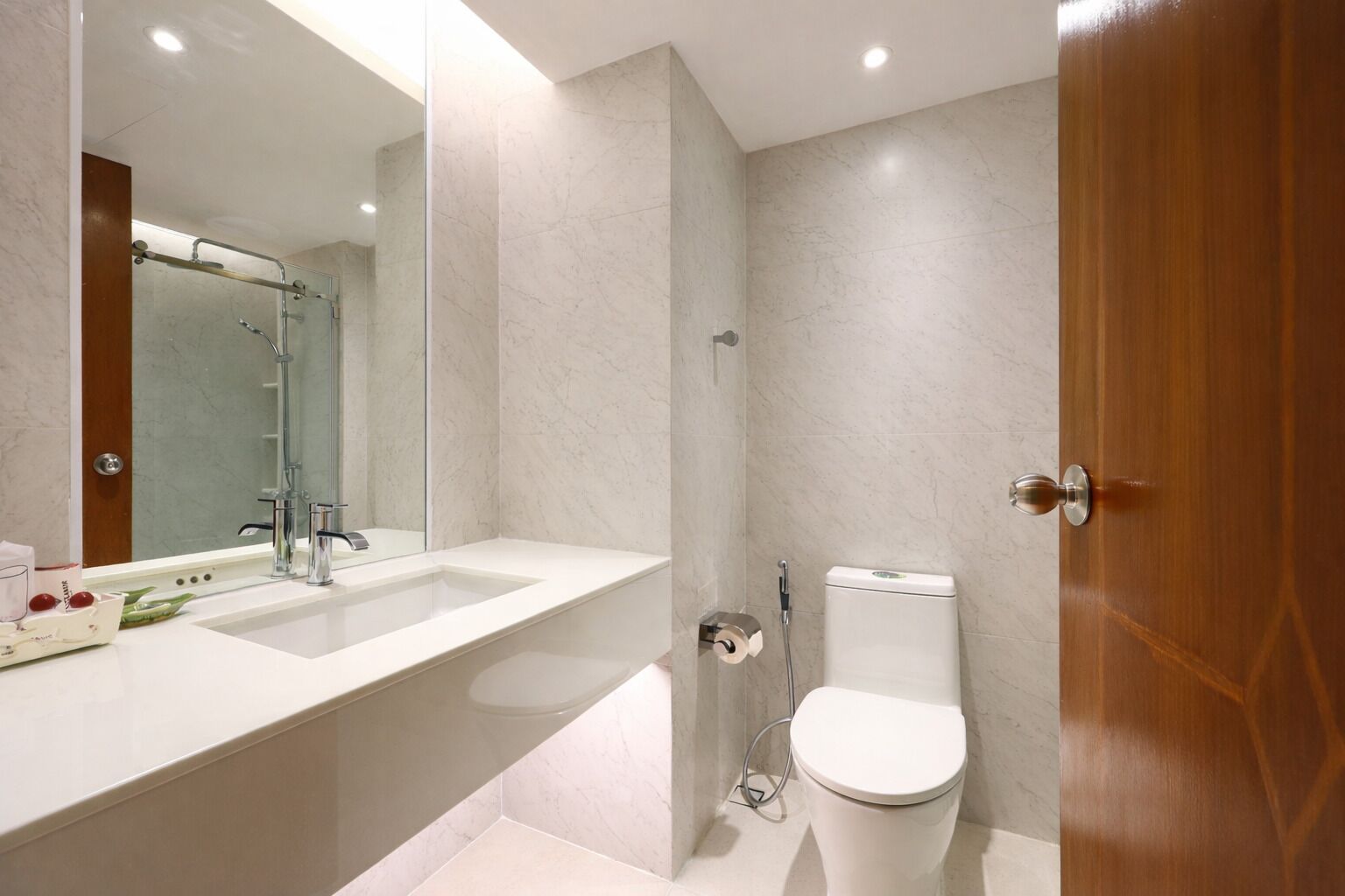 A modern bathroom with a large mirror, two sinks, a toilet, and a shower.
