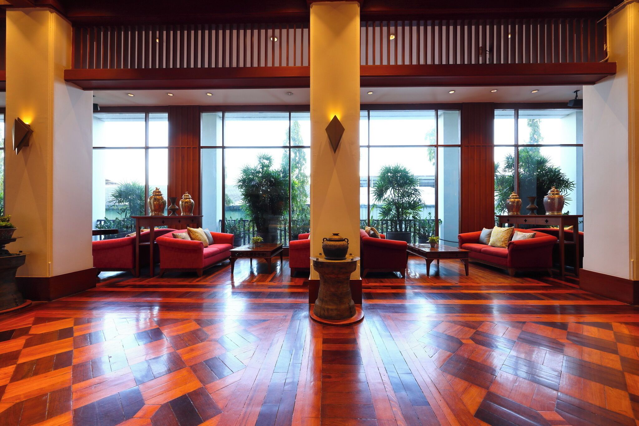 A spacious lobby with a checkered wooden floor, red sofas, and large windows offering a view of greenery outside.