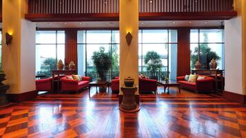 A spacious lobby with a checkered wooden floor, red sofas, and large windows offering a view of greenery outside.