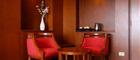 A room with two wooden chairs with red cushions, a small wooden table, and a vase with flowers on a shelf.