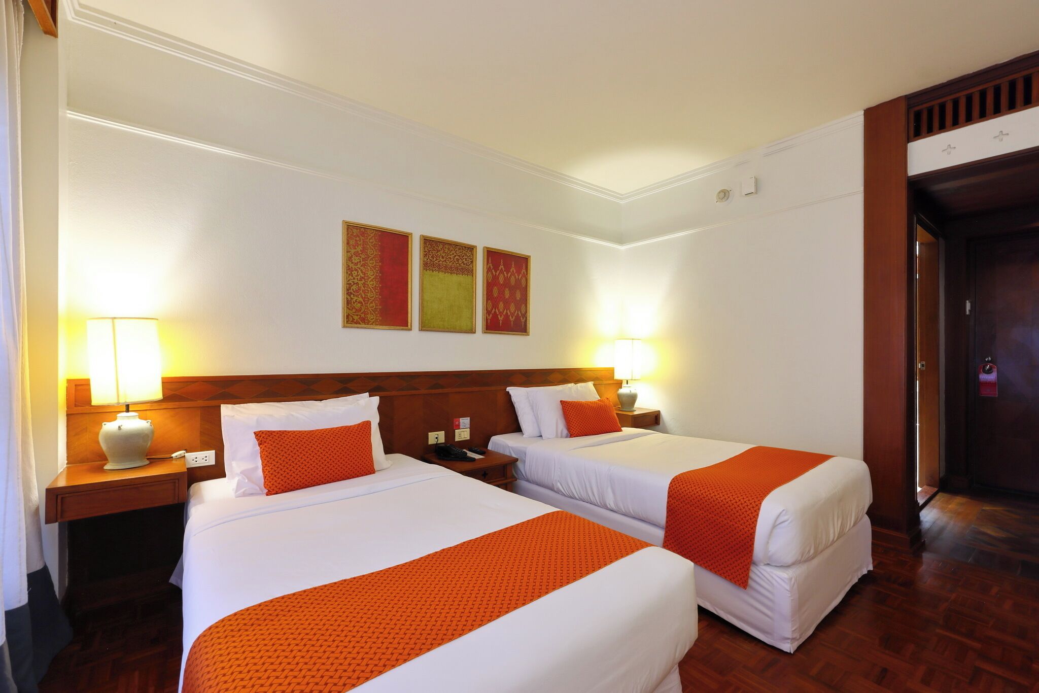 Una habitación de hotel con dos camas, un cabecero de madera, una mesita de noche con una lámpara y una puerta.