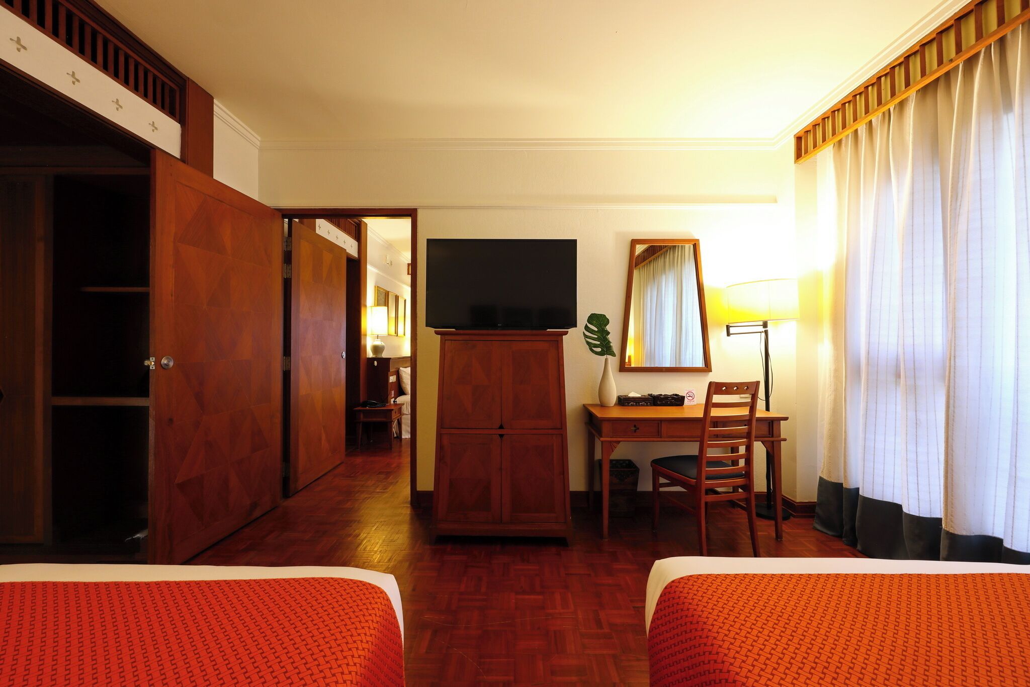 A hotel room with two beds, a desk, a television, and a dining area.