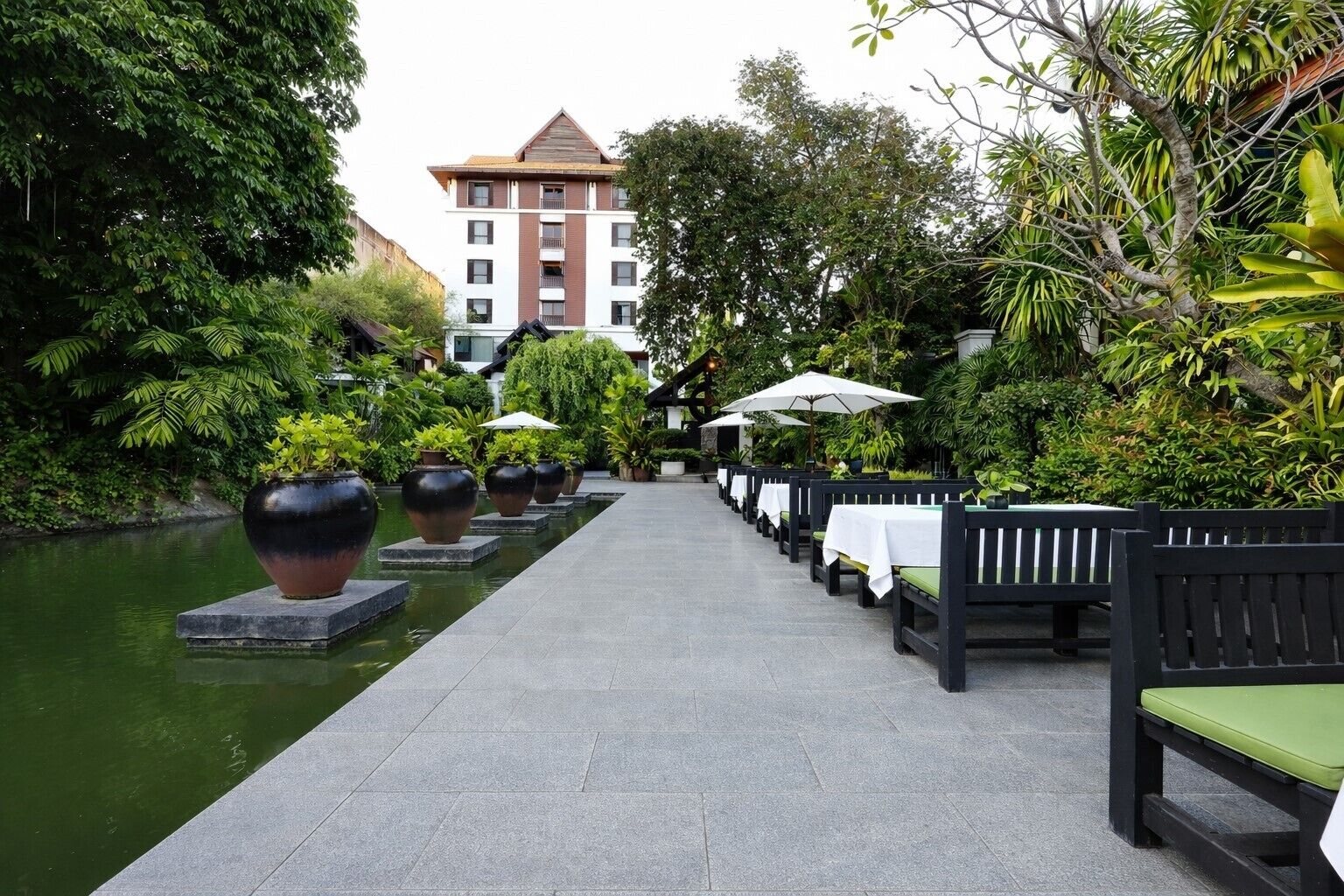 A pathway lined with tables and chairs, a water feature, and a building in the background.